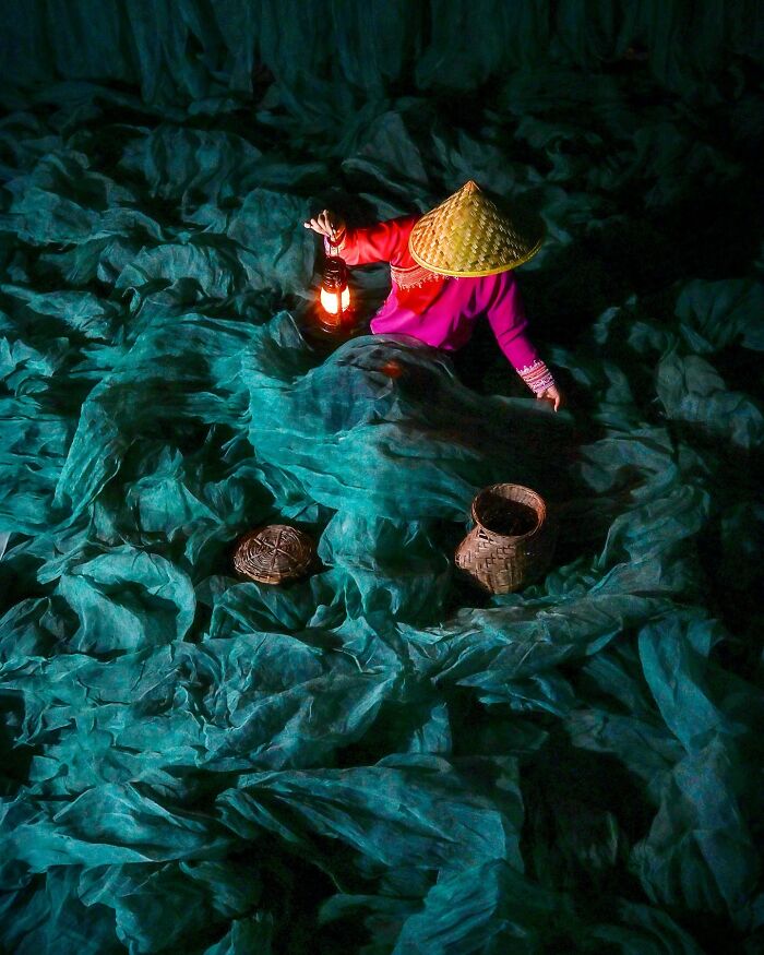 Asian woman in traditional hat holding a lantern amid green fishing nets, capturing the soul of Asia in a stunning photo.