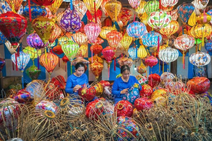 Two women crafting vibrant traditional lanterns in an Asian market, showcasing the soul of Asia through colorful art.
