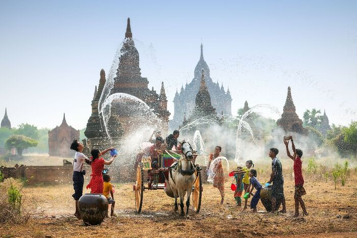 Children splash water joyfully near ancient Asian temples while a horse cart passes by, capturing the soul of Asia.