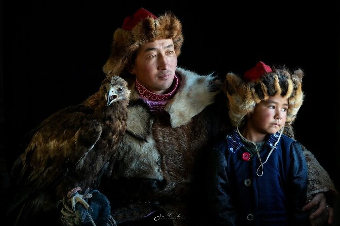 Two people in traditional fur hats with a large eagle, capturing the soul of Asia in a stunning portrait.