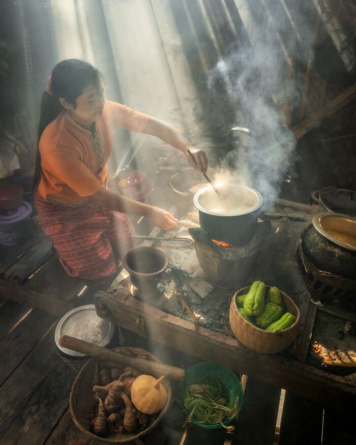 Asian woman cooking over a traditional stove with sunlight streaming in, capturing the soul of Asia in a stunning photo.
