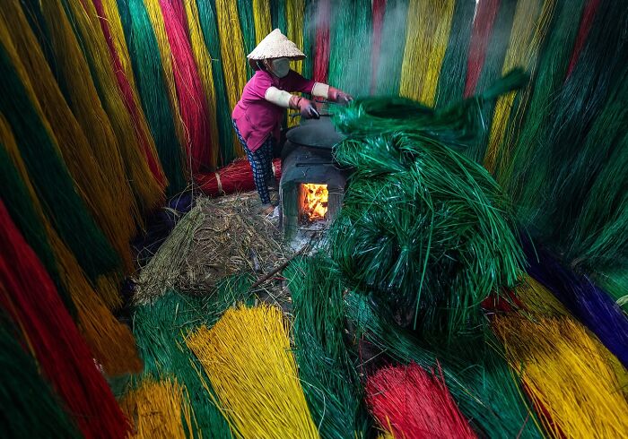 Worker in a traditional Asian workshop surrounded by vibrant colored threads, capturing the soul of Asia through stunning photos.