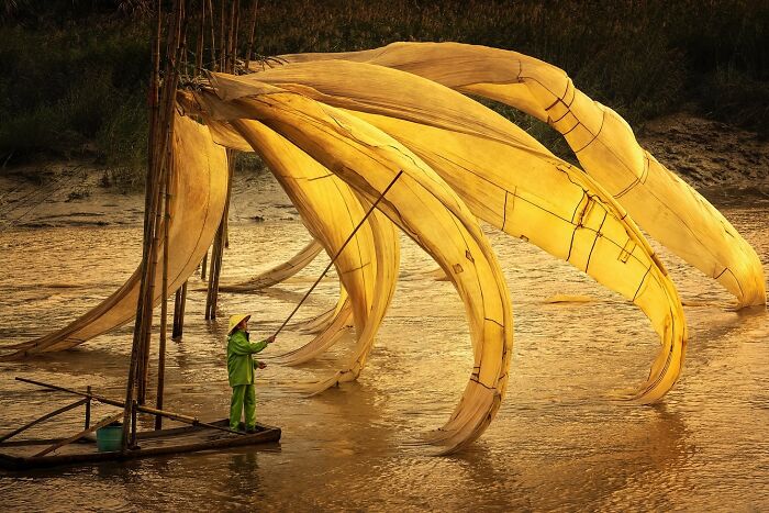 A photographer captures the soul of Asia with a fisherman in green using traditional large yellow fishing nets at sunset.