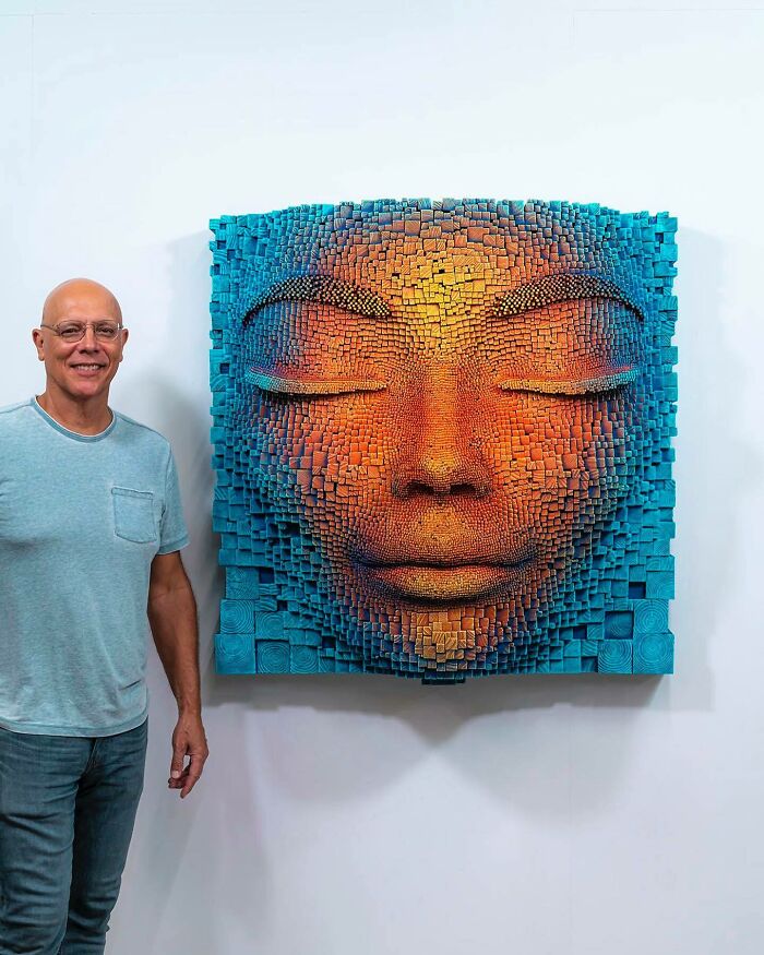 Sculptor standing next to a hypnotic 3D wooden face artwork made of small wooden sticks with vibrant colors.