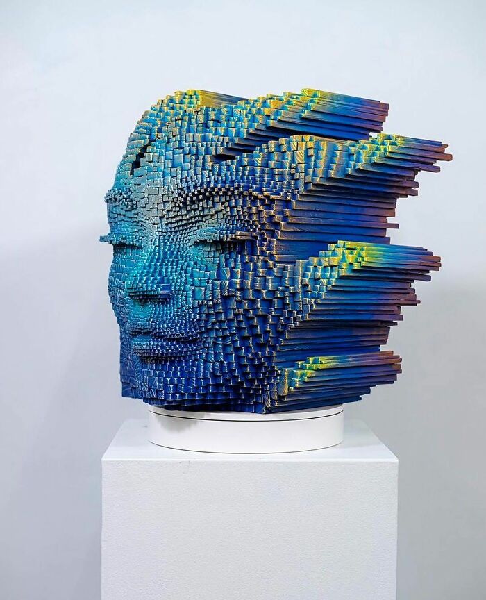 3D face sculpture made from wooden sticks, painted blue with yellow highlights, creating a hypnotic and alive effect.