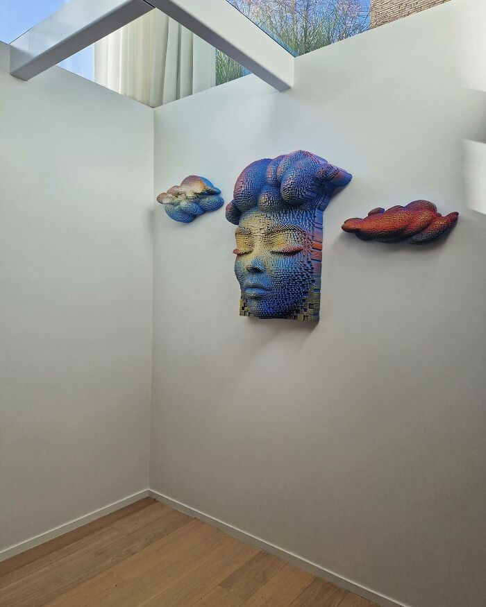3D wooden face sculpture and wooden cloud art mounted on a white wall in a minimalist room with skylight.