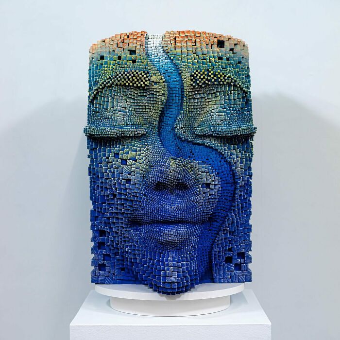3D face sculpture made from wooden sticks, featuring hypnotic details and vibrant blue and green colors.