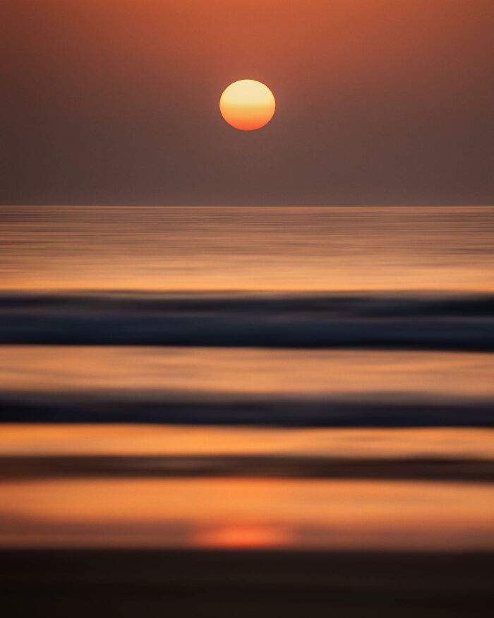 Sunset over calm ocean waves creating breathtaking landscape shot with warm orange and dark hues.