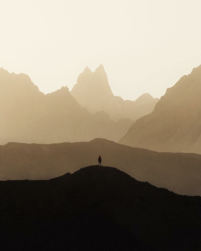 A person standing on a hill with breathtaking landscape shots of dramatic mountain peaks in a fantasy-like scene.