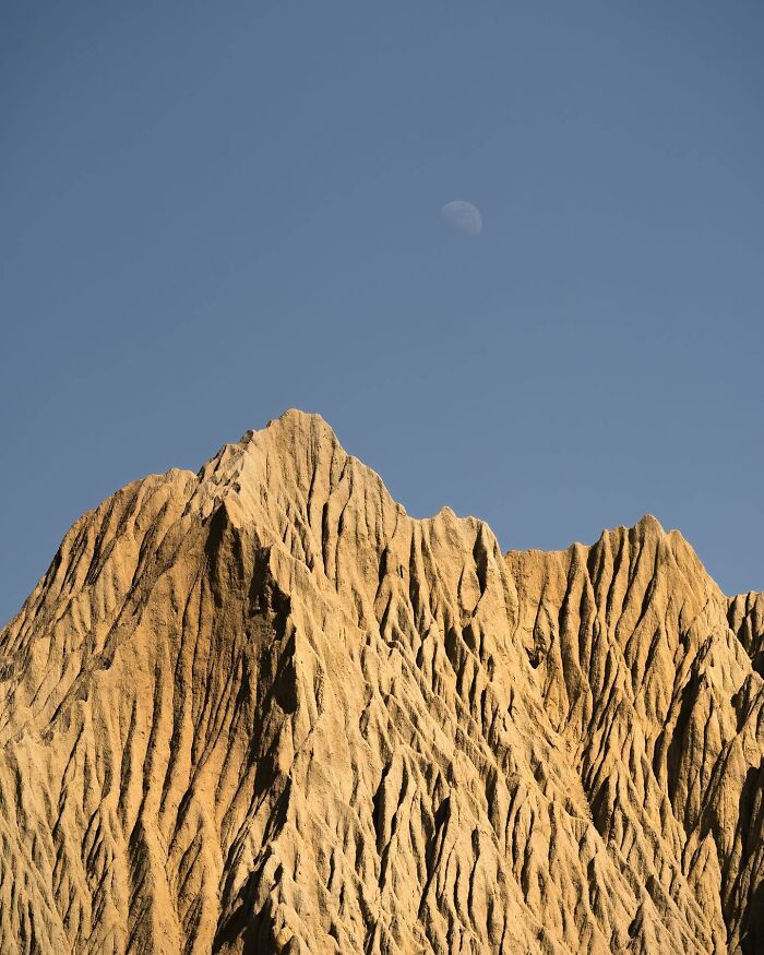 Jagged mountain peak with detailed textures under a clear sky and a visible moon in a breathtaking landscape shot.