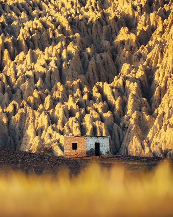 Small house in front of breathtaking landscape formations resembling a fantasy movie setting at golden hour.