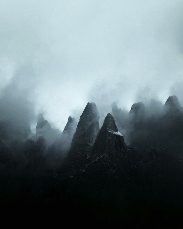 Dark jagged mountain peaks rising through thick mist, showcasing breathtaking landscape shots with a fantasy movie-like atmosphere.