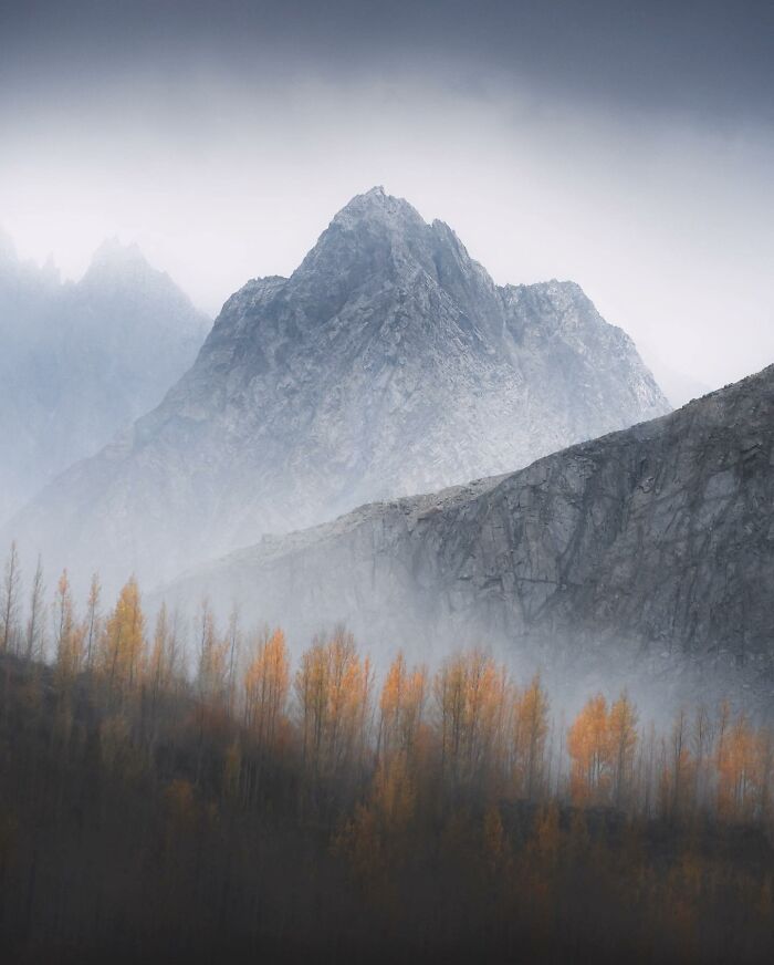 Misty mountain landscape with autumn trees in foreground, showcasing breathtaking fantasy-like scenery captured by photographer.