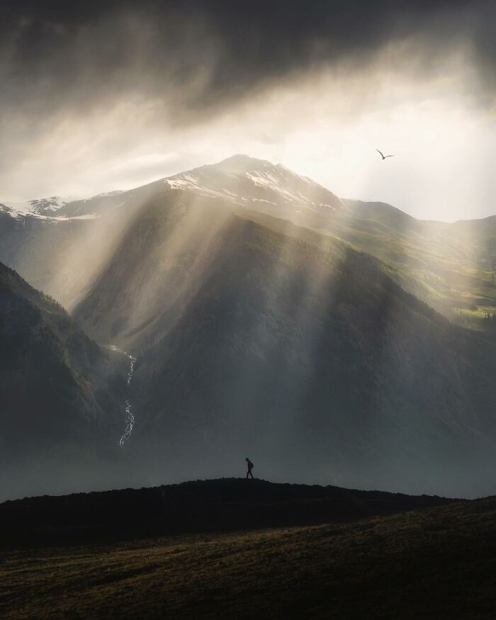 Breathtaking landscape with dramatic light rays over mountains and a lone figure, capturing a fantasy movie-like scene.