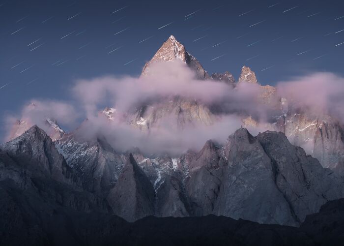Breathtaking landscape with jagged mountain peaks partially covered by mist under a starry twilight sky.