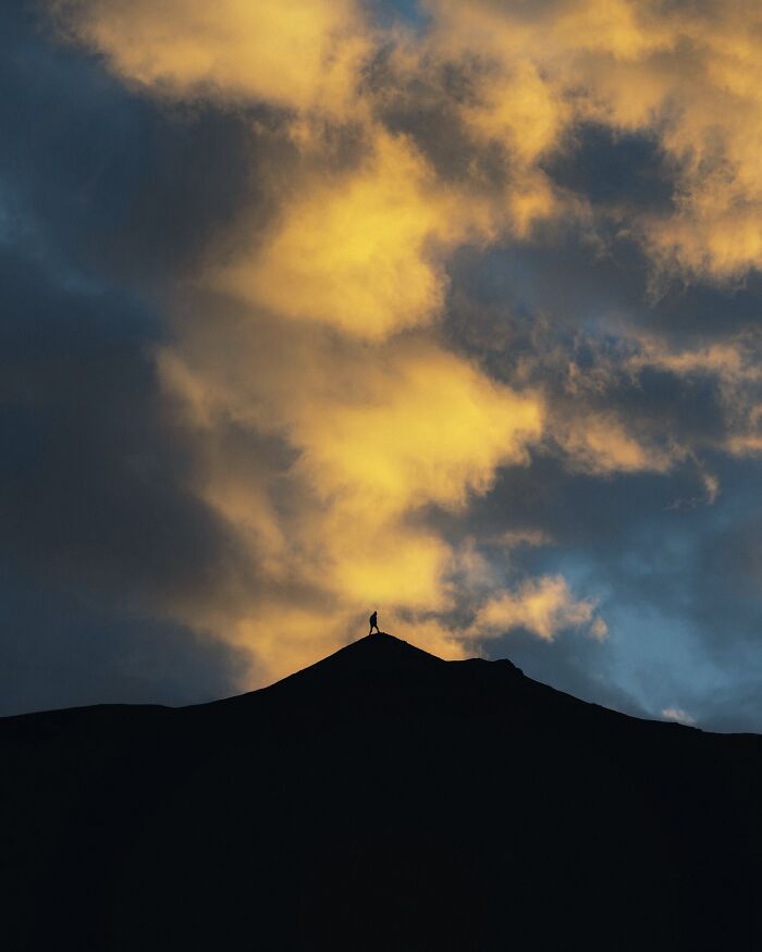 Silhouette of a person standing on a mountain peak under dramatic clouds in a breathtaking landscape shot.