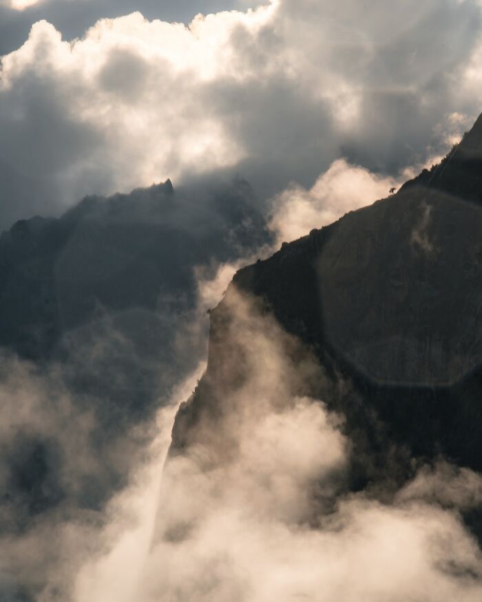 Misty mountain landscape with clouds and light rays creating a breathtaking fantasy movie-like scene.