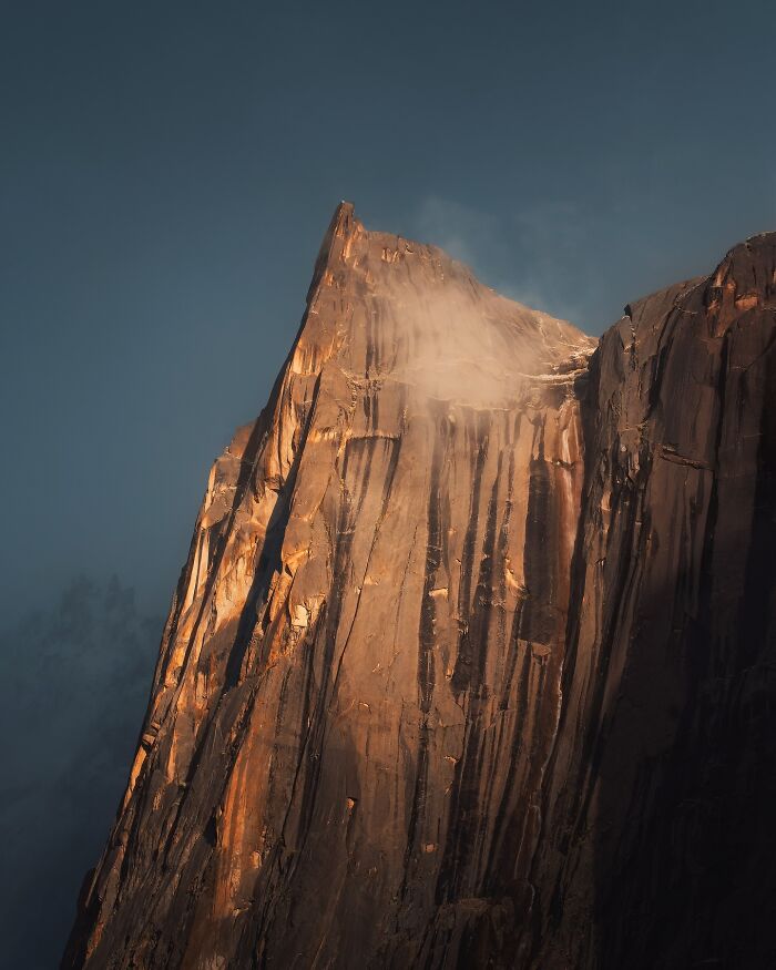 Breathtaking landscape shot of a towering mountain peak bathed in golden light with mist against a clear sky.