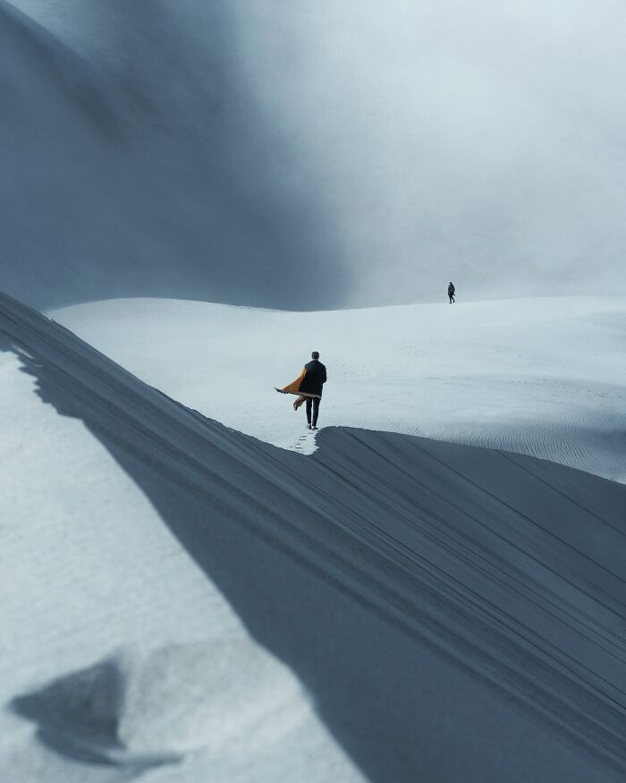 Two people walking across vast, breathtaking landscape dunes captured in a fantasy movie-like setting with dramatic light and shadows.