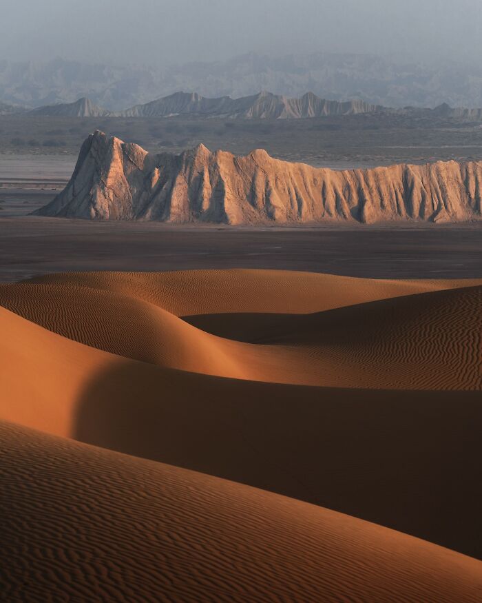 Breathtaking landscape of desert dunes with rugged mountain formations in soft light, resembling a fantasy movie scene.