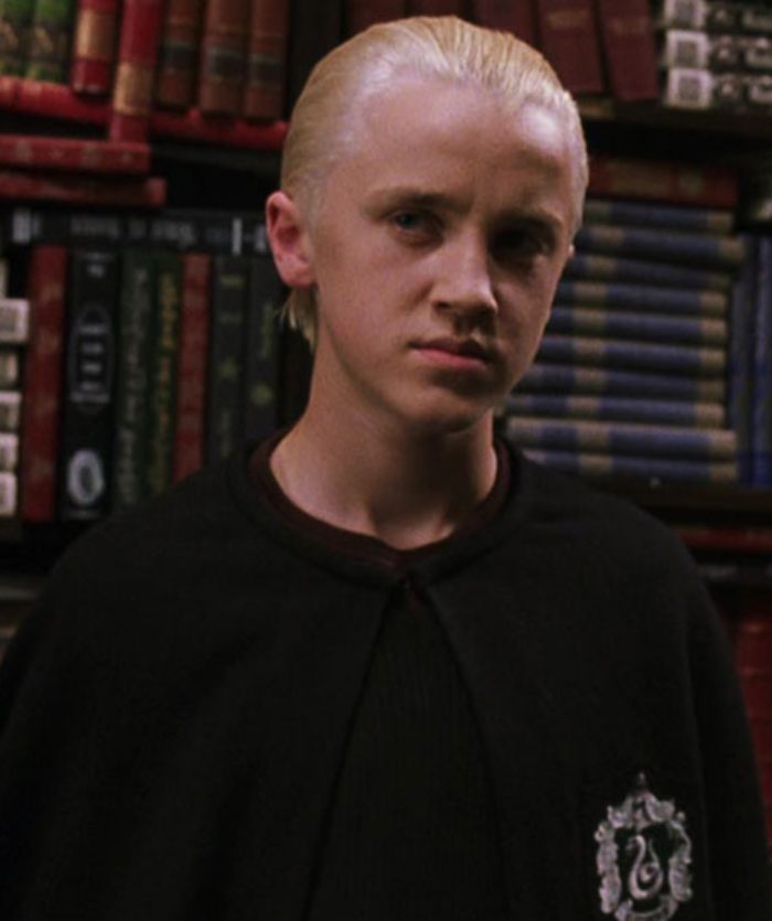 Actor dressed as Draco Malfoy from Harry Potter standing in front of a bookshelf during a surprise reunion with Harry Potter stars. Actor dressed as Draco Malfoy from Harry Potter standing in front of a bookshelf during a surprise reunion with Harry Potter stars.