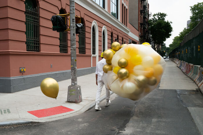 Photographer captures coincidental moment of a person walking with gold and white balloons on a city street.