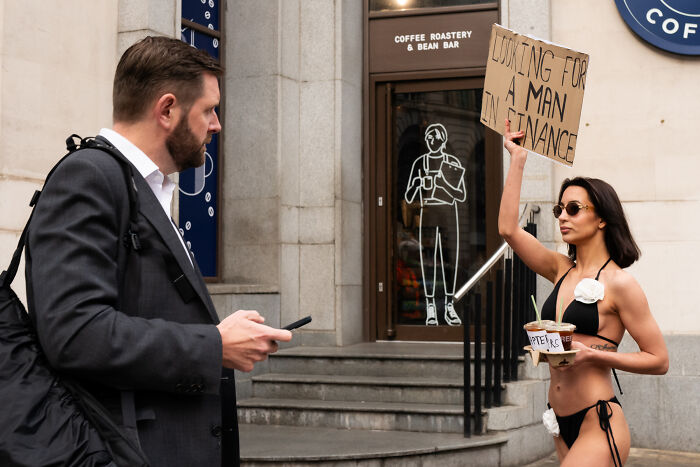 Photographer captures coincidental moment of a man with phone and woman holding a sign outside coffee roastery in public.