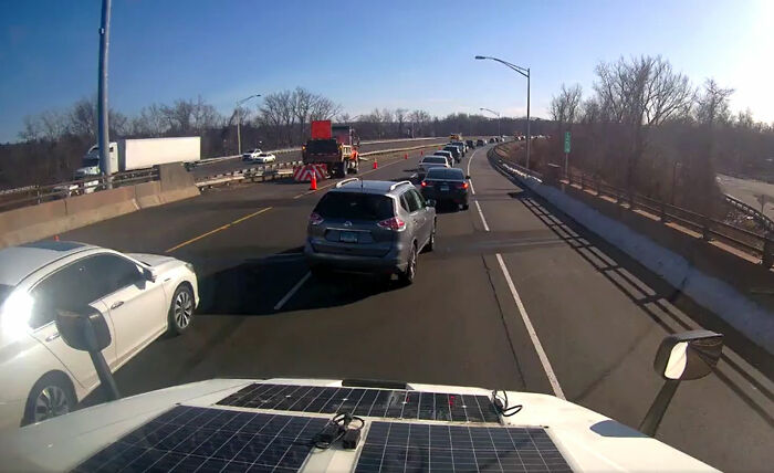 View from a vehicle of cars communicating calmly through lane merging on a sunny highway with traffic cones ahead.