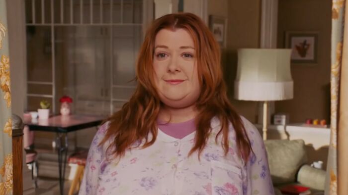 Actress in a floral pajama top standing in a cozy living room scene from one of the worst movies of all time.