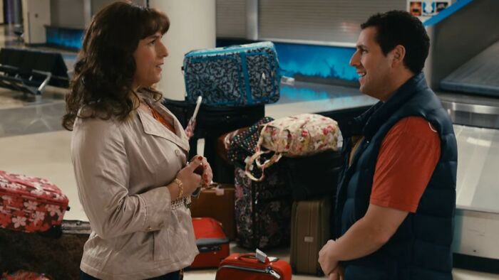 Two people talking in an airport with multiple colorful suitcases highlighting the worst movies of all time theme.