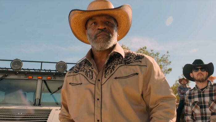 Actor in cowboy hat and western shirt stands in front of truck, scene representing worst movies from the hall of shame.