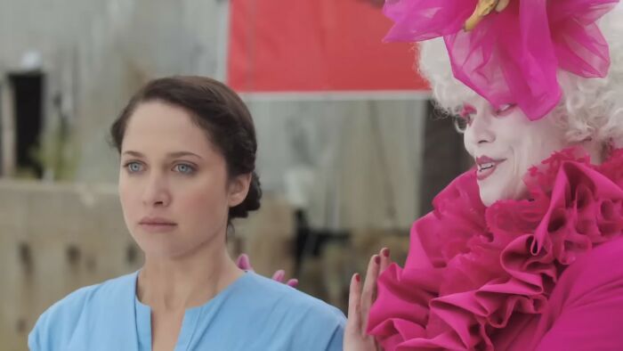 Woman in blue dress looking serious beside a person in elaborate pink costume representing worst movies of all time.