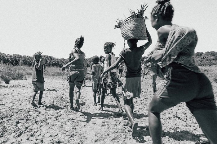 Children walking barefoot through a sandy mangrove area carrying baskets in a black and white mangrove photography image.