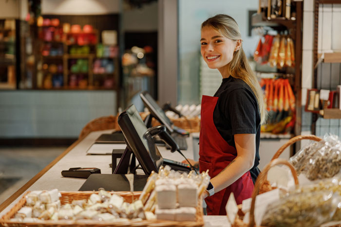Smiling employee in a red apron standing at a checkout counter, highlighting ableist manager workplace accommodation issues.