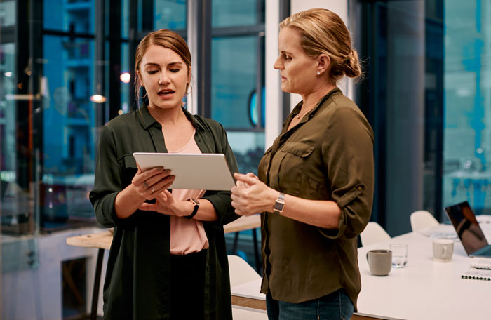 Two women in an office discussing on a tablet, depicting interaction between a manager and a disabled employee.