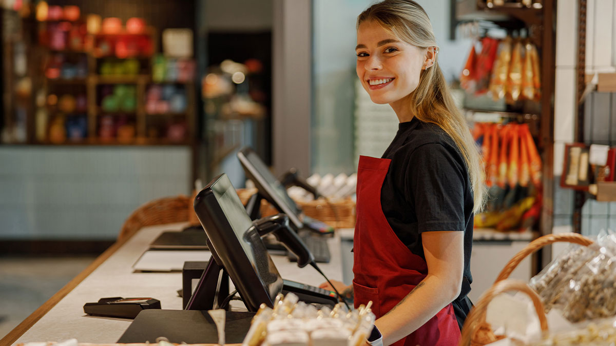 Young female employee smiling at checkout in store, representing ableist manager and disabled employee workplace issues.