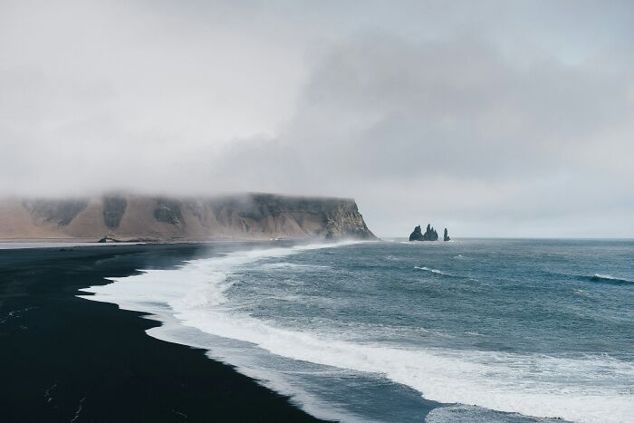 Coastal landscape with black sand beach and cliffs under cloudy sky, representing smartest countries shaping the future.