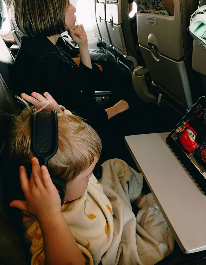 Child wearing headphones watching tablet on airplane, highlighting plane passenger frustration over seat dispute. Child wearing headphones watching tablet on airplane, highlighting plane passenger frustration over seat dispute.