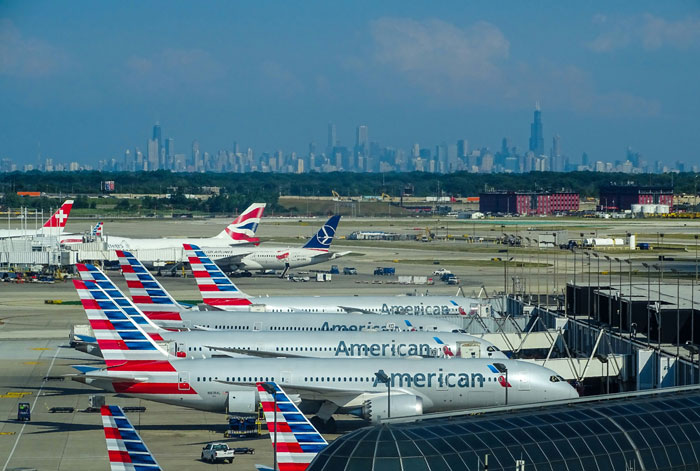 American Airlines planes lined up at airport gates with city skyline in background, related to plane passenger seat dispute. American Airlines planes lined up at airport gates with city skyline in background, related to plane passenger seat dispute.