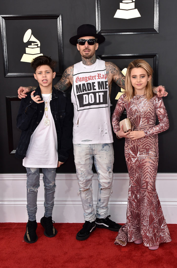 Man and two children posing on a red carpet event, highlighting Alabama Barker’s net worth backed by generations of fame.