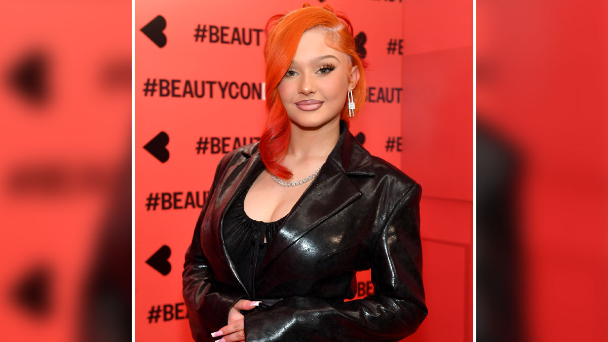 Alabama Barker posing at Beautycon event with bright orange hair and black leather jacket, showcasing her self-made net worth.
