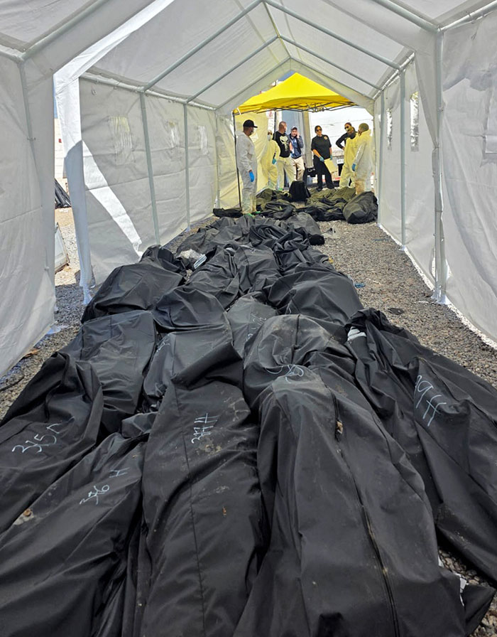 Black body bags stacked inside a tent with forensic investigators and police officers examining the scene, human bodies discovery. Black body bags stacked inside a tent with forensic investigators and police officers examining the scene, human bodies discovery.