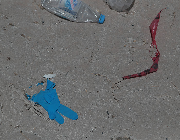 Blue discarded glove and plastic bottle on sandy ground at site linked to cops discovering human bodies. Blue discarded glove and plastic bottle on sandy ground at site linked to cops discovering human bodies.