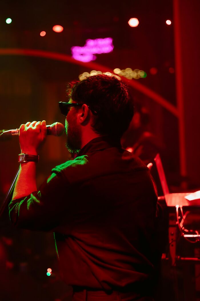 Man wearing sunglasses singing into a microphone on stage with colorful lights capturing arrogant people moment.
