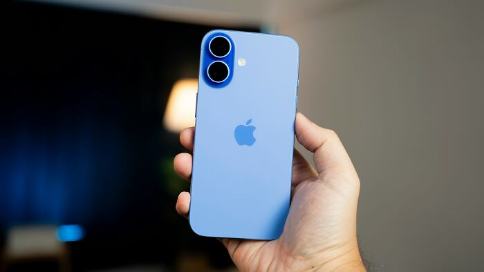 Hand holding a blue iPhone against a blurred background illustrating trends leading to overconsumption concerns.