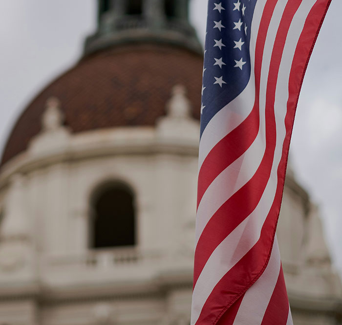 American flag waving in front of a historic building symbolizing a man threatening to explode plane mid-flight incident. American flag waving in front of a historic building symbolizing a man threatening to explode plane mid-flight incident.