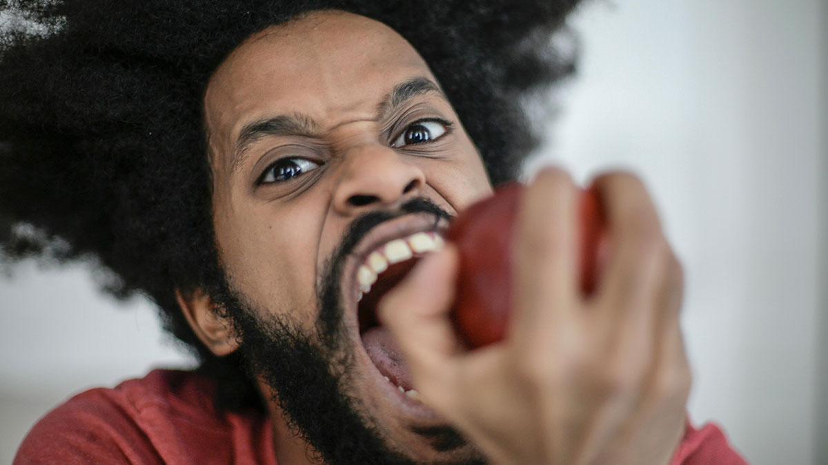 Man with intense expression biting into a red apple, illustrating annoyed chewing sounds related to psychiatric disorder.