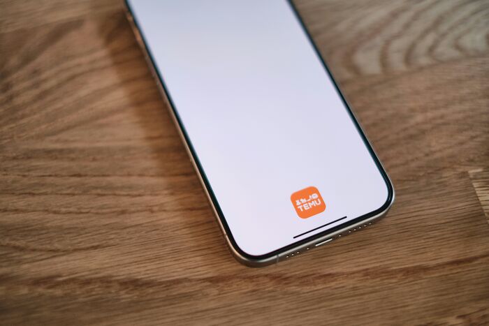 Smartphone displaying a shopping app on a wooden surface, illustrating trends leading to overconsumption.