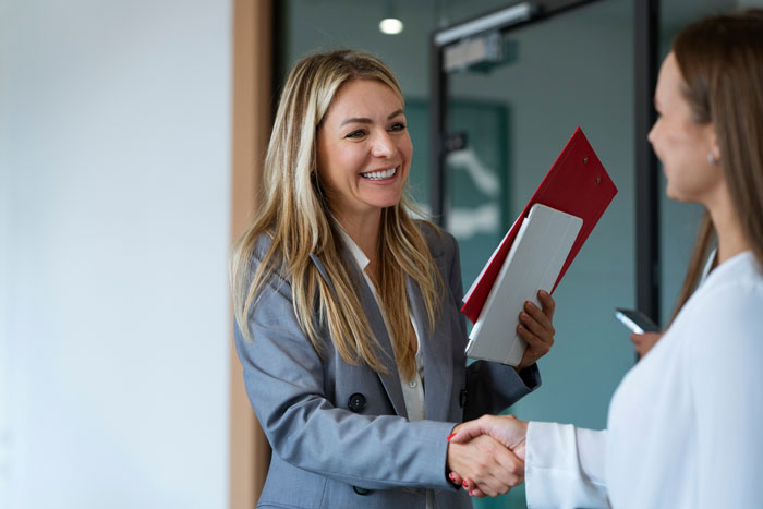 Two professional women shaking hands in office, discussing asking husband to turn down dream job career decision. Two professional women shaking hands in office, discussing asking husband to turn down dream job career decision.