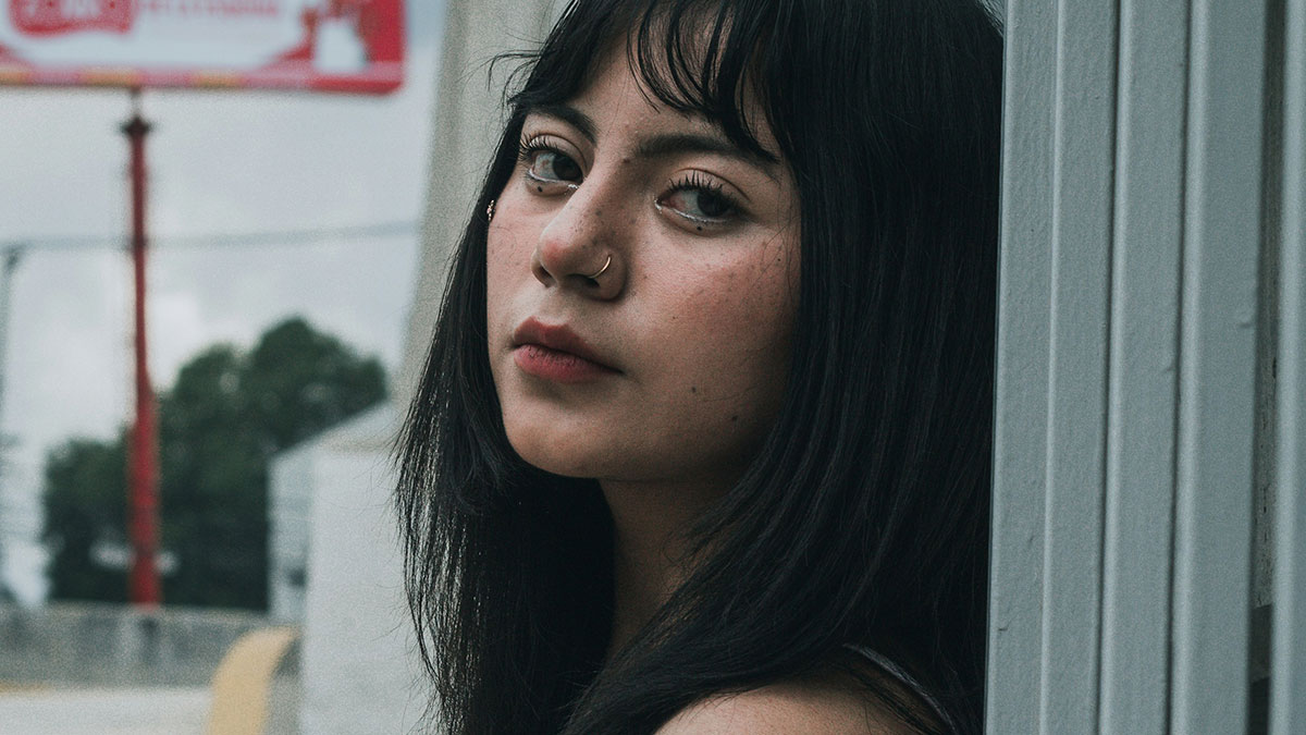Young woman with dark hair and nose ring leaning against a wall, expressing a calm and introspective mood for sociopath topic